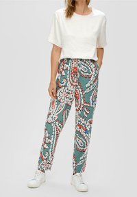 Biały, teksturowany top z krótkim rękawem w parze z luźnymi, wzorzystymi spodniami w kolorze teal, zdobionymi czerwonymi i białymi kwiatowymi motywami. Całość dopełniają białe tenisówki.