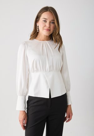 Blusa bianca a maniche lunghe con tessuto arricciato sulle spalle e un davanti plissettato. Presenta una vita aderente e un orlo dritto.
