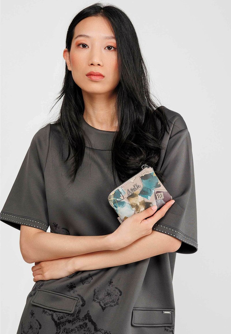 Top gris de manga corta con detalles de tachuelas, combinado con una cartera de patrón multicolor con diseños florales y cierre de cremallera.