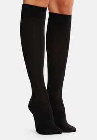 Knielange schwarze Socken aus glattem Stoff mit einem gerippten Bündchen oben. Sie haben eine taillierte Form und keine sichtbaren Muster oder Designs.