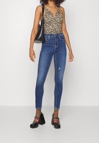 Bolso de cuero negro, body de estampado de leopardo, jeans ajustados azules, calcetines de estampado colorido y tacones gruesos negros. Diseño texturizado y ajustado.
