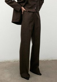 Pantaloni in misto lana marroni con una silhouette a gamba larga, vita alta e cuciture eleganti, abbinati a un blazer aderente coordinato.