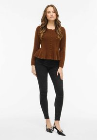 Rudos flanelinės suknelės tipo megztinis su sagomis, ilgomis rankovėmis ir tekstūruota medžiaga, derinamas su juodais siaurėjančių kojų džinsais ir siaurų kulnų bateliais.