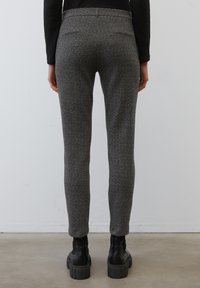 Pantalons gris à chevrons avec une coupe slim, présentant une taille haute et un dos sans couture. Portés avec des bottes noires à semelle épaisse. Texture de tissu lisse.