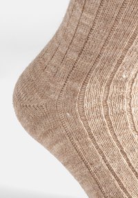 Calcetín de punto en color beige claro con una textura acanalada y un patrón sutil. Presenta un talón reforzado para mayor durabilidad.
