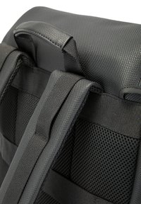 Mochila gris con un exterior sintético texturizado, respaldo de malla acolchada, correas ajustables y un asa superior para un fácil transporte.