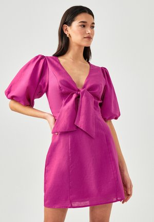 Abito corto fucsia con scollatura a V profonda, maniche a palloncino e dettaglio a fiocco frontale. Realizzato in un tessuto lucido con una texture liscia e una forma aderente.