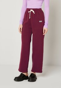 Burgundijas sporta bikses ar aukliņu jostasvietā, sānu kabatām un izšūtu "American Vintage" logo. Gluda kokvilnas auduma, brīva piegriezuma.