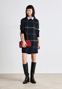 Marinblå rutig klänning med gröna och röda detaljer, kombinerad med knähöga svarta läderstövlar och en liten röd handväska.