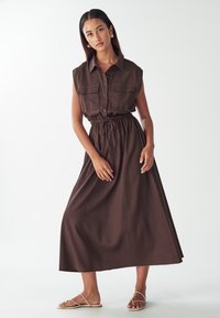 Hnedé maxi šaty bez rukávov s predným zapínaním na gombíky, dvoma vreckami na hrudi, elastickým pásom a voľným strihom. Hladká tkanina a dlhý dizajn až po zem.