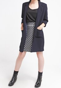 Laivastonsininen pitkä bleiseri, musta toppi, musta-valkoinen kuviolaukku, nilkkapituiset mustat nauhakengät, joissa on kiinteät mustat sukat.