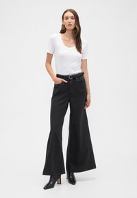 Jeans pretos de perna larga com cintura alta e passantes para cinto, combinados com um top branco justo de mangas curtas. Tecido liso e ajuste casual.