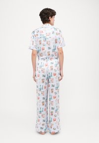 Ensemble de pyjama à motifs comprenant des manches courtes et un pantalon large. Le tissu est léger, avec une palette de couleurs pastel et des images décoratives.