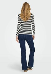 Un haut à rayures noir et blanc à manches longues associé à un jean évasé bleu foncé. La tenue présente une coupe classique et un design décontracté.