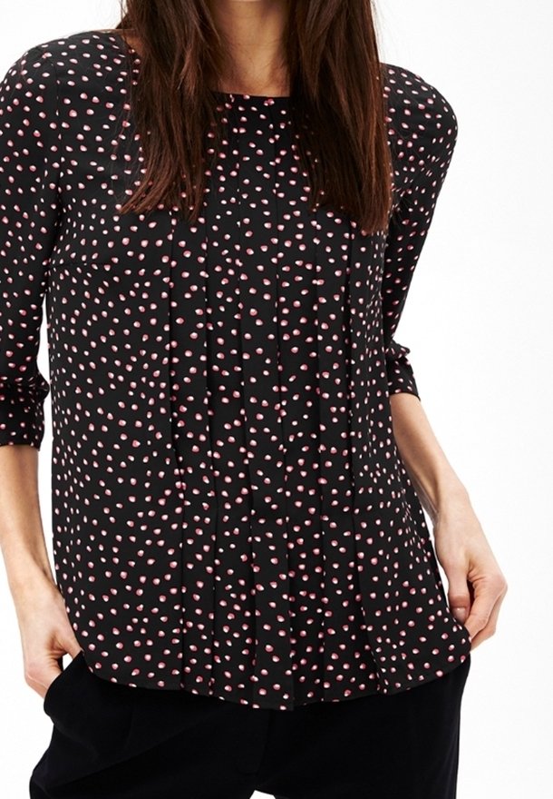 Blusa nera con pois rosa, con davanti plissettato, scollo rotondo e maniche a tre quarti. Realizzata in un tessuto leggero e liscio.