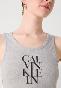 Pilkas medvilninis sansiukas su juodu grafiniu tekstu "CALVIN KLEIN", kuris yra centriniu būdu išdėstytas. Apvalus kaklas su švariu apdailu.