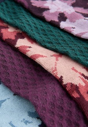 Quatre échantillons de tissu tricoté de couleurs variées : bordeaux, vert, pêche avec motif et lavande ; surfaces texturées et à motifs visibles.