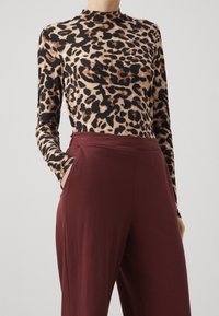 Leopardmönstrad långärmad topp i mjukt tyg med hög halsringning, kombinerad med hög midja bordeauxfärgade byxor med fickor.