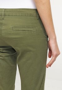 Olive green cotton trousers with a smooth texture, featuring a back pocket and a straight cut. Minimalist design with tailored stitching.