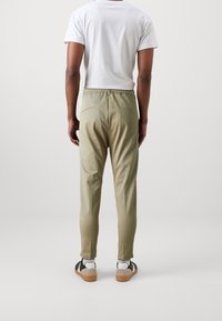 Spodnie oliwkowe z elastycznym paskiem w dopasowanym kroju, z dwiema tylnymi kieszeniami. W zestawie z białymi skarpetami do kostki i czarnymi trampkami.