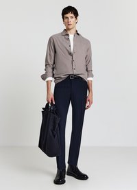 Camicia grigia con bottoni, maglietta bianca sotto, pantaloni scuri su misura, stivaletti neri alla caviglia, porta una borsa tote scura con diverse tasche.