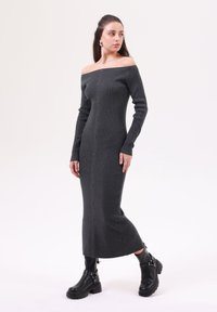 Mörkgrå off-shoulder stickad klänning med långa ärmar, med en knappslå framtill. Kombinerad med svarta ankelboots som framhäver en smickrande silhuett.