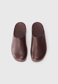 Sabots en cuir marron avec une texture lisse, un bout arrondi et un design à dos ouvert. Forme simple et minimaliste sans matériel visible ni motifs.