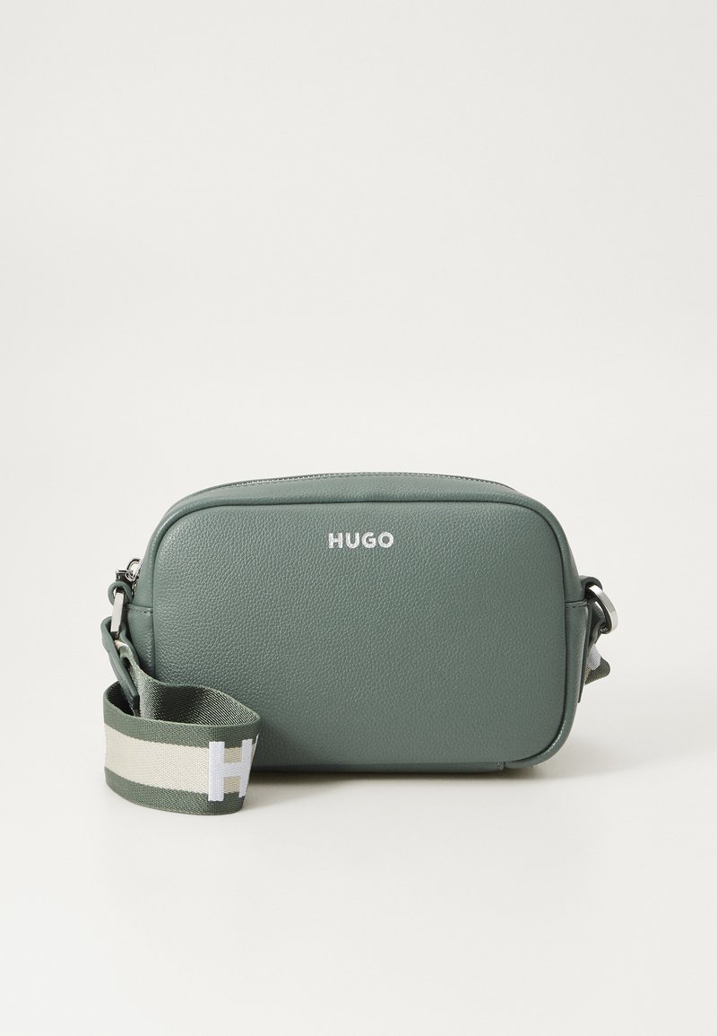Grønn lærcrossbody-bag med glidelåslukking, med en hvit "HUGO" logo og en stripete stoffrem i grønn og hvit.