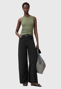 Top de tirantes ajustado verde oliva, pantalones de pierna ancha negro, cinturón negro, sandalias planas y un bolso de asas con estampado. Diseño simple, corte relajado.