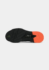 Semelle de chaussure de sport noire avec un motif texturé, ornée d'un accent orange et d'un logo vert. Conçue pour l'adhérence et les performances.
