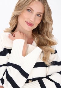 Cardigan a strisce bianche e blu navy in maglia con texture a costine, ampio colletto e dettagli con bottoni dorati. Le maniche presentano accenti a taglio.