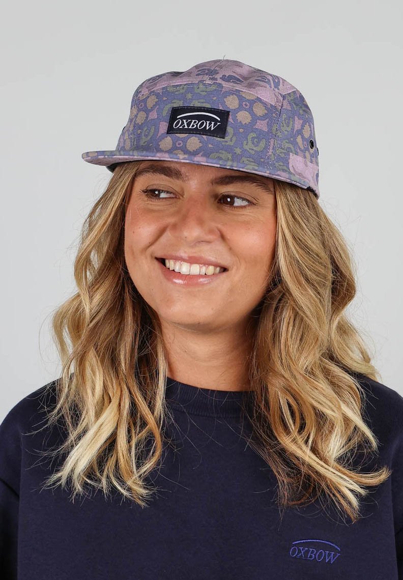 Casquette camo violette avec des motifs circulaires et des accents de couture. Présente un label Oxbow noir sur le devant. Design à visière plate.