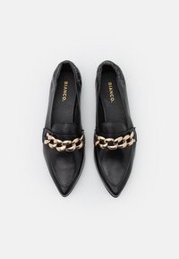 Chaussures en cuir noir à enfiler avec un bout pointu, dotées d'une accent en chaîne dorée à l'avant. Texture lisse avec des bords élastiques.
