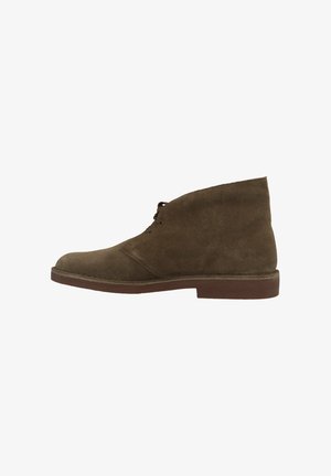 Brown suede ankle boot with a rounded toe, lace-up front, and a straight, textured heel. Minimalist design with smooth surfaces.