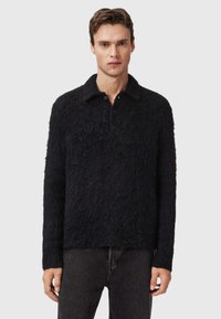 Un suéter negro peludo con cuello, que presenta un cierre de botones y mangas largas. Material texturizado y suave, con un dobladillo que llega a las caderas.