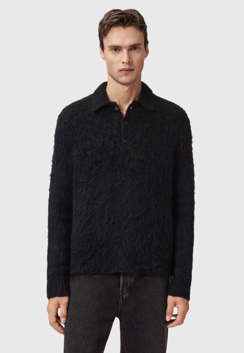Un suéter negro peludo con cuello, que presenta un cierre de botones y mangas largas. Material texturizado y suave, con un dobladillo que llega a las caderas.