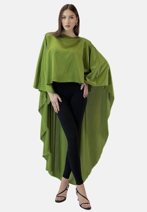 Cappa verde, fluente, con orlo asimmetrico, realizzata in tessuto leggero. Indossata sopra leggings neri, presenta maniche ampie e una consistenza morbida.