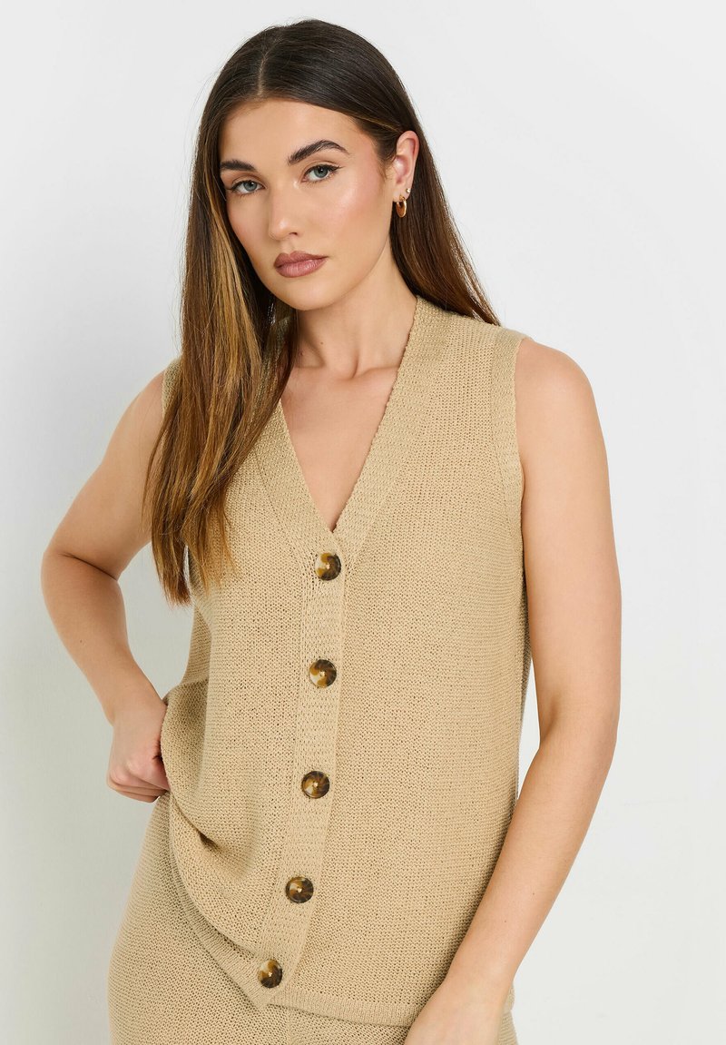 Beige stickad ärmlös väst med V-ringning och fem stora runda knappar fram. Texturerad tyg med sidfickor.
