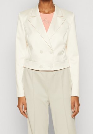 Femme portant un blazer croisé crème sur mesure, un top pêche et un pantalon crème taille haute assorti.