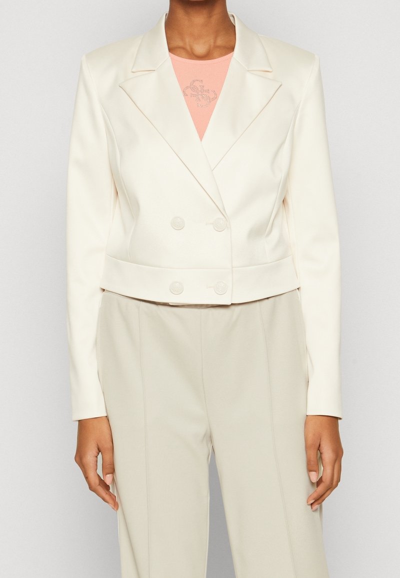 Femme portant un blazer croisé crème sur mesure, un top pêche et un pantalon crème taille haute assorti.
