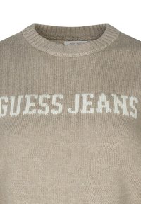 Maglione beige lavorato a maglia con colletto tondo, caratterizzato da testo "GUESS JEANS" in bianco, tessuto testurizzato e colletto e polsini a coste.