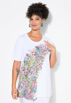 Tunique blanche fluide avec un design floral coloré d'un côté ; elle possède un col arrondi et des manches courtes, fabriquée en tissu léger.