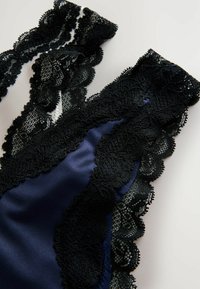 Body in satin blu navy con rifiniture in pizzo, con dettagli in pizzo nero lungo i bordi, caratterizzato da un design a scollo a V e accenti a ondulazione.