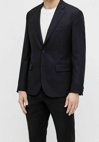 Granatowa marynarka z klapą w kształcie notch, z zapięciem na jeden guzik i dwoma przednimi kieszeniami. Gładki materiał z dopasowanym fasonem, noszona na białej koszuli.