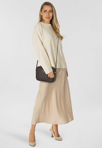 Jersey de punto crema, falda de satén beige y tacones altos color nude. Bolso cruzado negro con textura lisa y diseño minimalista.