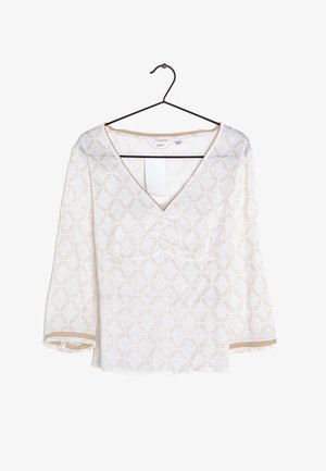 Weiße Bluse mit beigem geometrischem Muster, V-Ausschnitt und Dreiviertelärmeln, die an einem schwarzen Kleiderbügel vor einem weißen Hintergrund hängt.