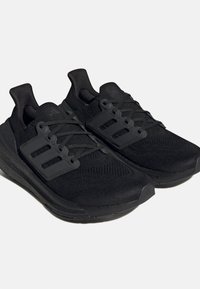 Paire de baskets de sport noires avec dessus en maille, trois bandes sur les côtés, semelles rembourrées et fermeture à lacets sur fond uni.