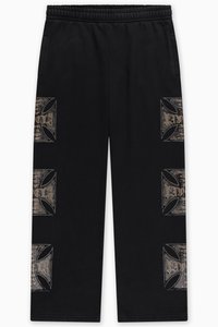 Black sweatpants feature an elastic waistband, side pockets, and distinct graphic patterns in a distressed gold finish on the sides.