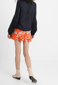 Granatowa bluzka z bufkowymi rękawami i haftowanymi detalami, zestawiona z pomarańczową spódnicą w kwiatowy wzór oraz beżowymi botkami na czarnym obcasie.