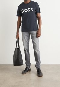 Mörkblå bomulls t-shirt med vit "BOSS" text, grå jeans, svart läderhandväska och svarta sneakers med grå detaljer.